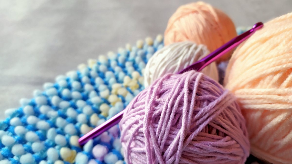 Colorful yarn, crochet hook, and textured crochet fabric.