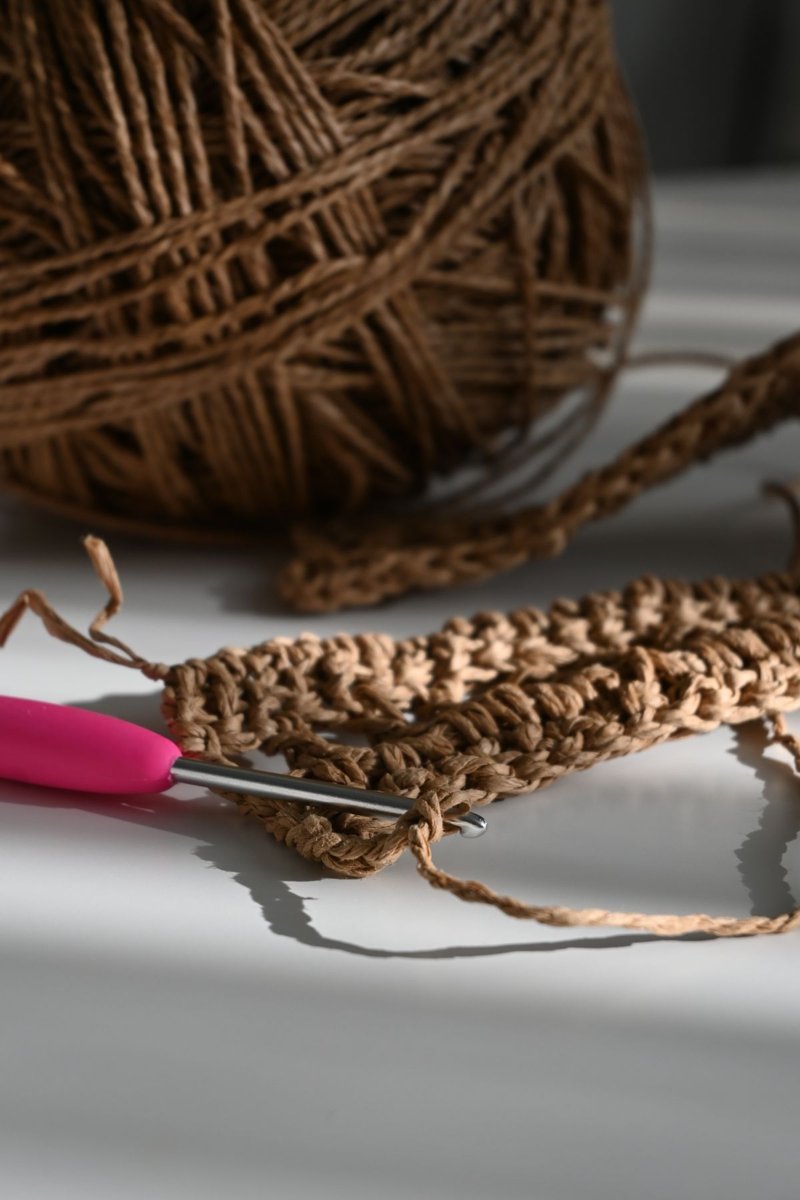 A crochet hook beside a textured work in progress.