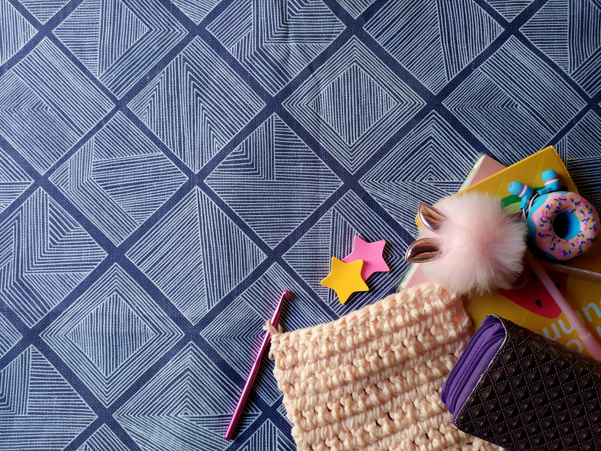Crochet hook, yarn, and pattern notes on a blue work surface.